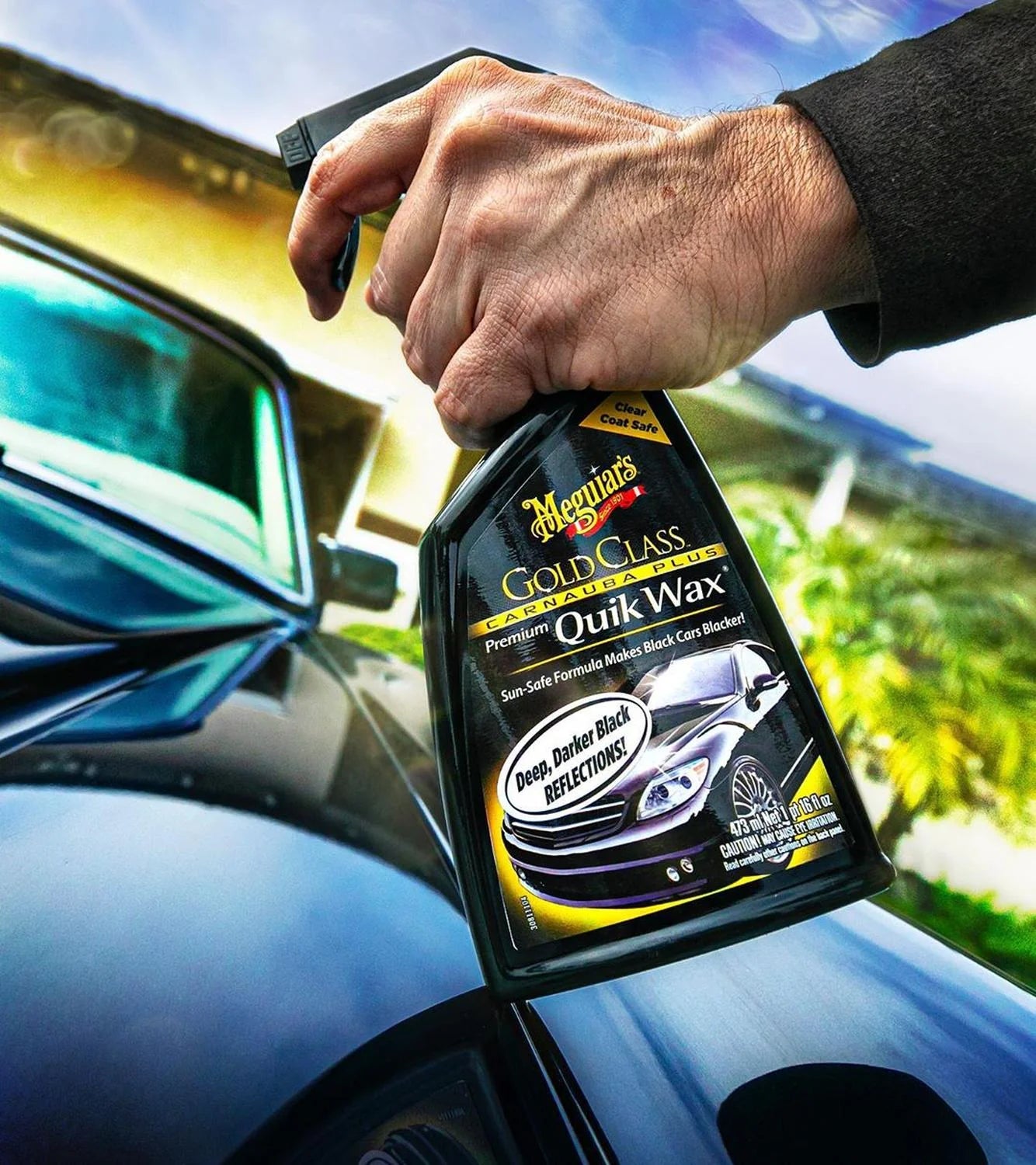 Hand holding a bottle of Meguiar's Gold Class Quik Wax in front of a car.