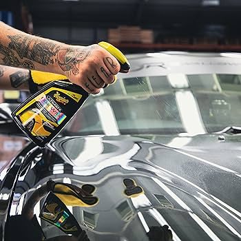 Person applying a product to a car window with a yellow spray bottle.