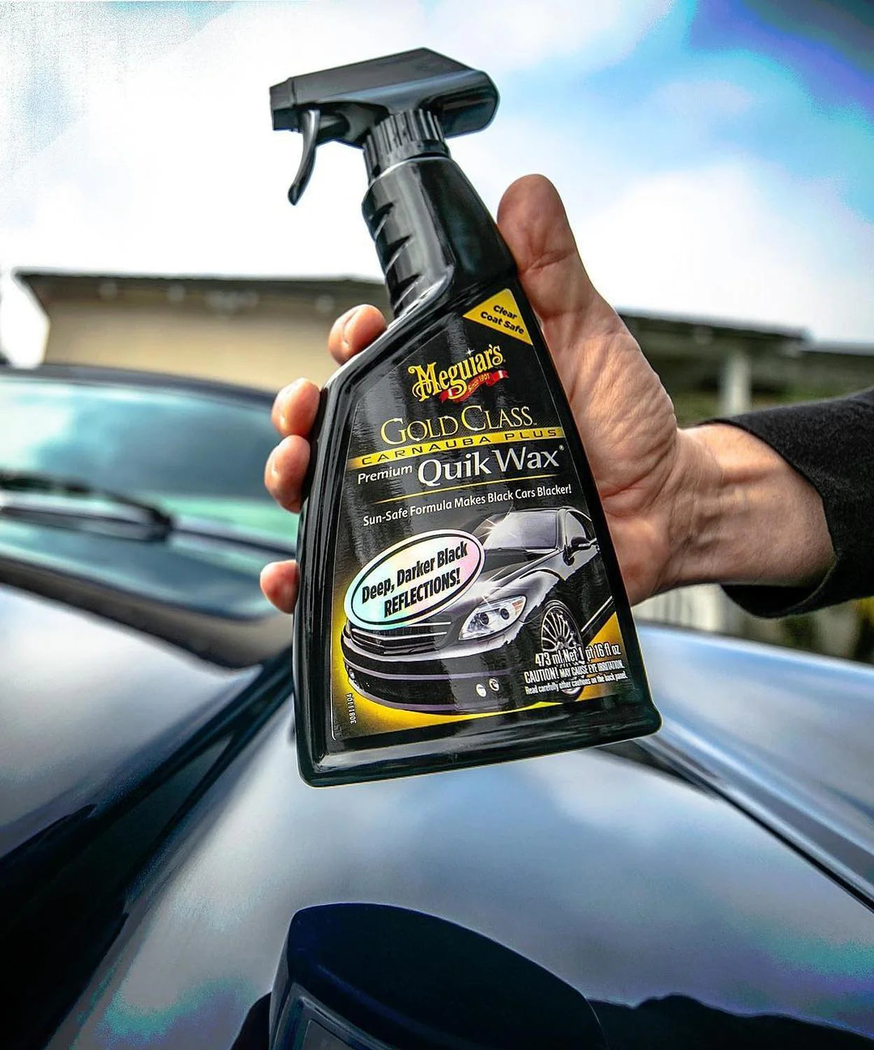 Hand holding a Meguiar's Gold Class Quik Wax car care product with a car in the background